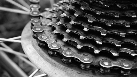 A close-up B&W image showcasing the intricate mechanics of bike gears, highlighting the chain, cassette, and derailleurs.