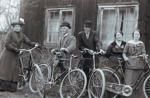 Black and white photo from the 1910s featuring a group of people in Sweden. Two gentlemen and three women are standing next to their bicycles.