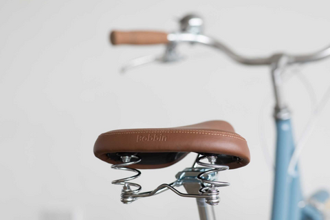 Un gros plan d'une selle de vélo en cuir en relief avec "Bobbin". Le reste du vélo bleu en arrière-plan