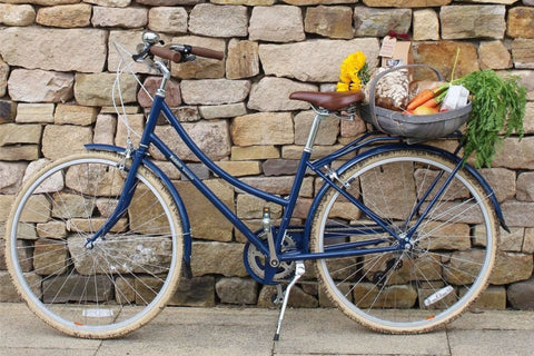 Blueberry Brownie Bike avec panier plein d'épicerie devant un mur de briques jaunes.