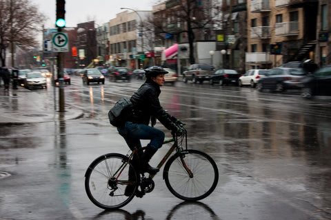 City commuter cyclist crossing a wet road, navigating urban streets in rainy weather.