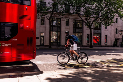 A person cycling in London behind the double decker bus