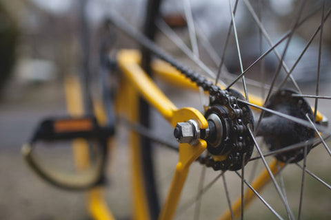 Close up picture of a yellow bike, showing the rear chain, spoke, and other parts.