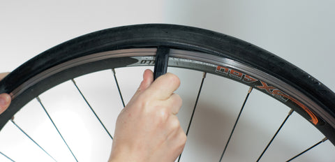 Eine Hand einer Person, die ein Reifenreparaturwerkzeug hält und den Schlauch des Fahrrads entfernt