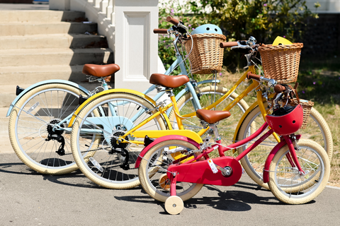 Drei Gingersnap-Kinderfahrräder in Blau, Gelb und Rot aufgereiht auf einem Bürgersteig.