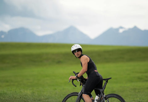 A male cyclist takes a serene break, leaning on his bike, surrounded by lush greenery and mountains in the background.