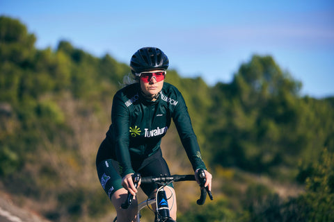 A woman in a green shirt and sunglasses riding a bike.