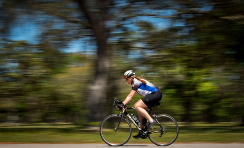 A woman cyclist accelerates with speed, creating a blur effect in the background.