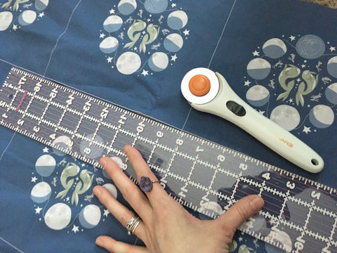 A person cutting a fabric with a mini cutting tool and a ruler