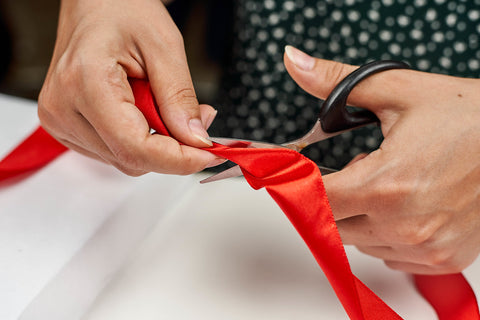 A hand of a woman cutting a red ribbon with a black scissor