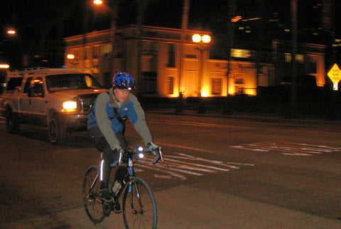 A cyclist riding on a highway at night, wearing a helmet with bike lights and reflective clothing.