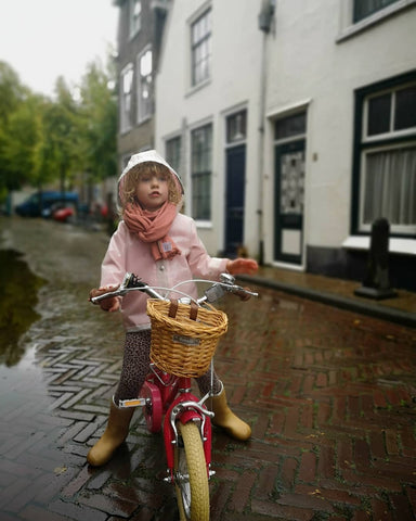 Kind radelt im Regen, Regenhut und Mantel