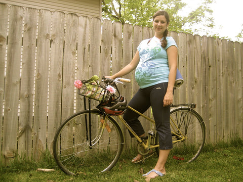 Pregnant woman at 32 weeks joyfully poses on her bicycle in a backyard setting.