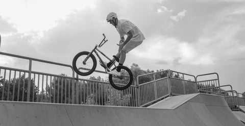 A grayscale photo of a man performing BMX bike tricks on-ramp.