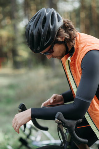 Man in orange vest and black cycling shirt with black helmet sitting on a bicycle