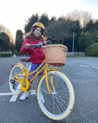 Mädchen auf gelbem Fahrrad mit Korb und passendem Helm