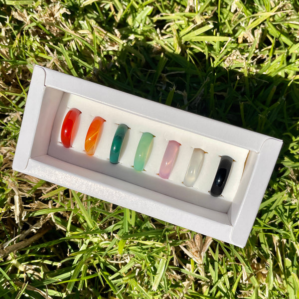 set of 7 chakra stone rings from whitestone jewelry co. lying on grass with open box