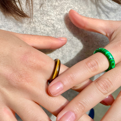 whitestone jewelry co. tiger eye and malachite stone band rings worn on different hands by woman in close up shot