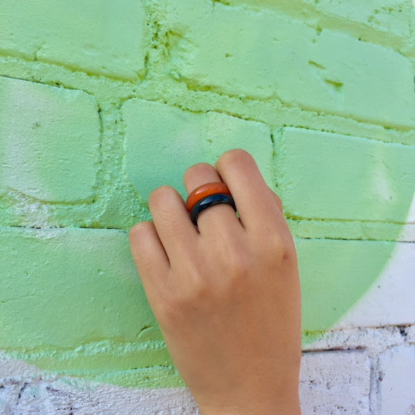 woman's hand against a green wall wearing the orange agate chakra ring from whitestone jewelry co. along with the black onyx ring