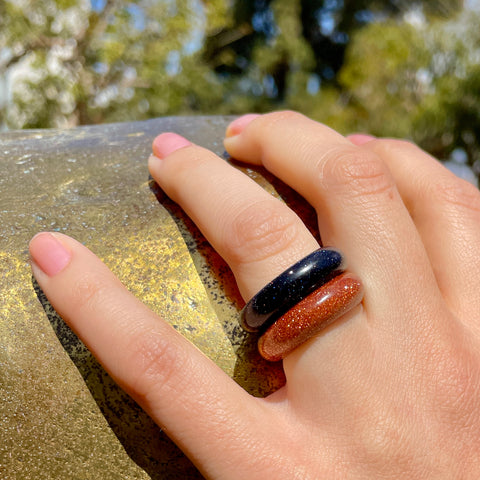 closeup of blue goldstone and gold goldstone band rings from whitestone jewelry co worn by woman on her same finger