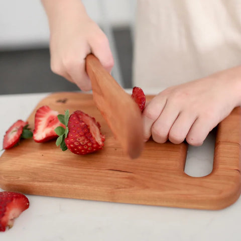 Child using a wooden cutting board and wooden knife