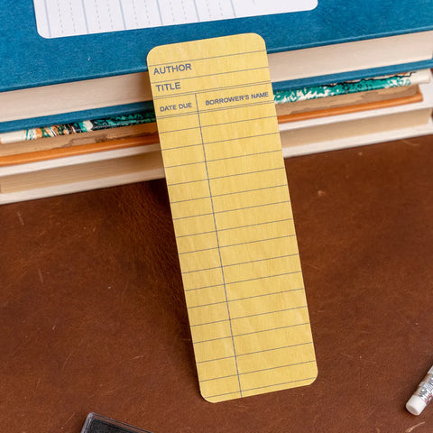 Yellow Library Card Bookmark displayed next to a stack of books at Laurel Mercantile Co