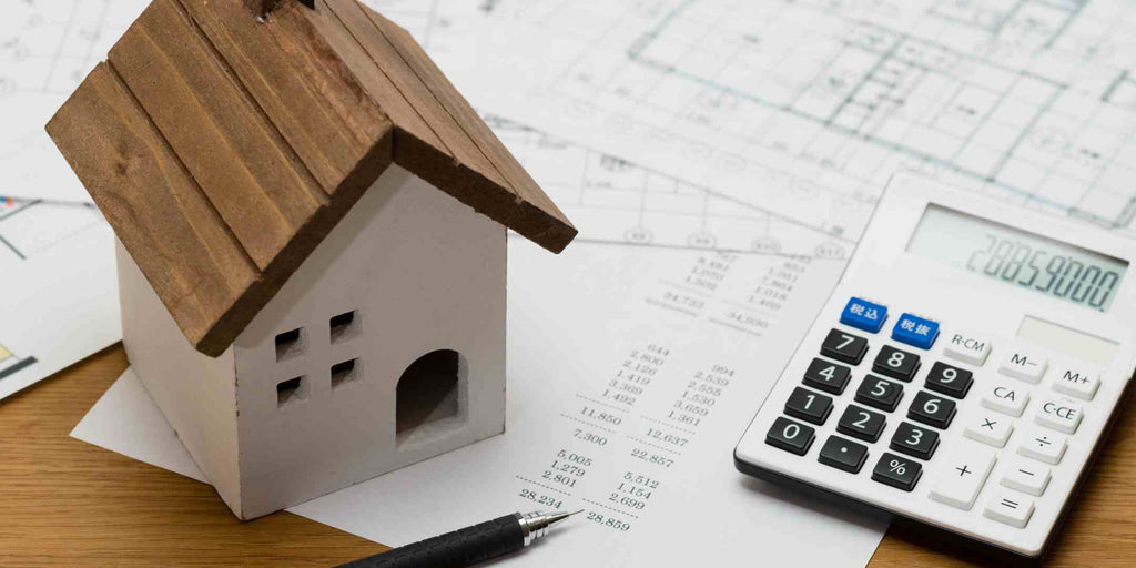 Image displaying a miniature house model, a calculator showing cost estimates, and a blueprint, all symbolizing the cost of renovating an HDB flat. The picture emphasizes the financial planning aspect of undertaking a renovation project.