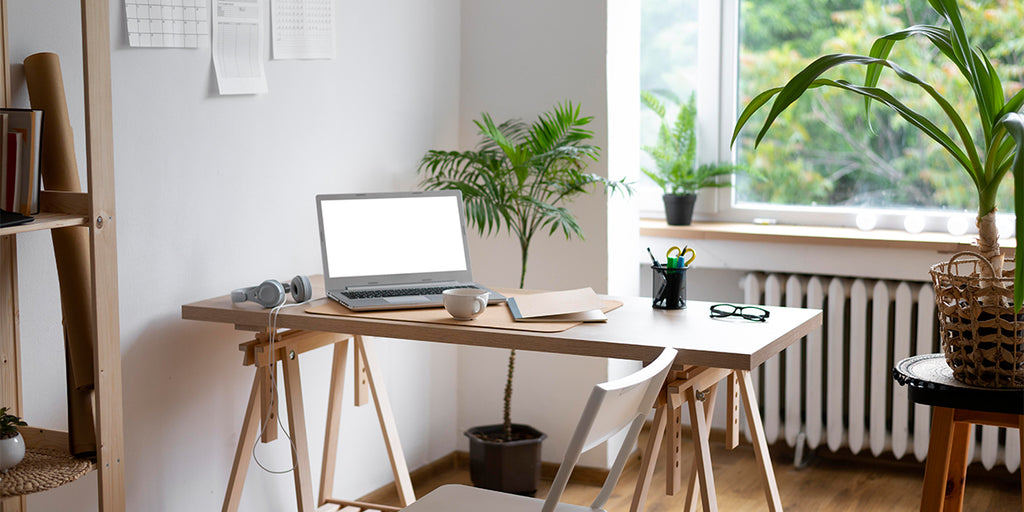 A home office space designed with Scandinavian principles, featuring large windows that let in plenty of natural light and indoor plants, creating a strong connection with nature. The workspace also includes sustainable wooden furniture and neutral tones, demonstrating the Scandinavian emphasis on functionality, simplicity, and respect for the environment.