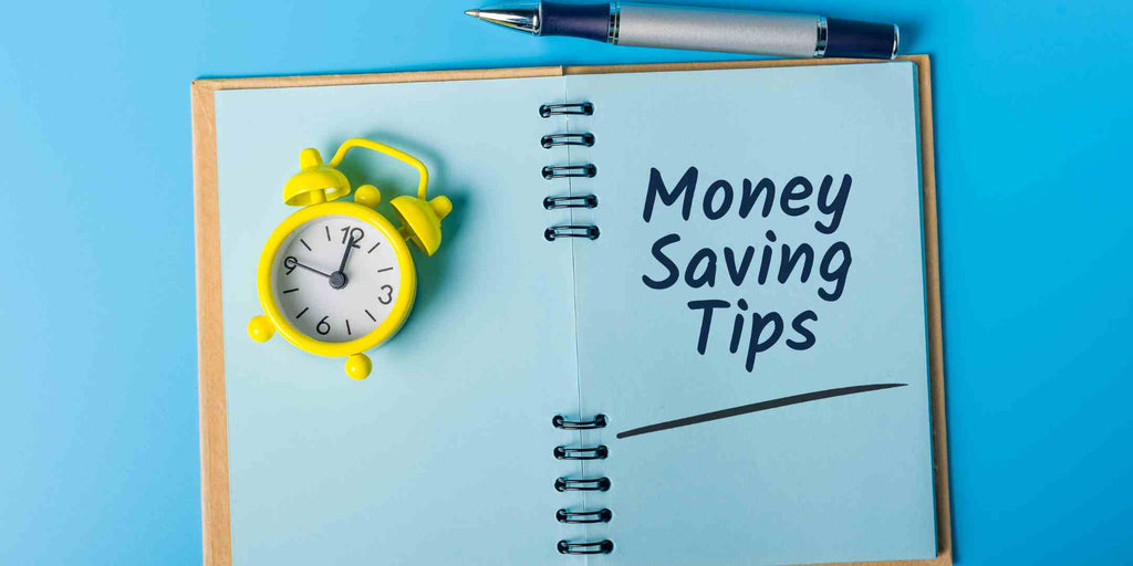 An image of a notebook opened to a page  with handwritten text money-saving tips, with a small clock resting beside it. The clock symbolizes the value of time management in planning and executing cost-effective strategies for home improvement.