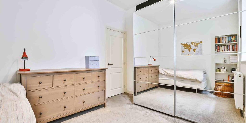 Image illustrating a small home renovation idea where mirrors are strategically used to create a sense of spaciousness. The picture shows a bedroom with a mirrored wardrobe that reflects the room, making it appear larger and more open than it actually is.