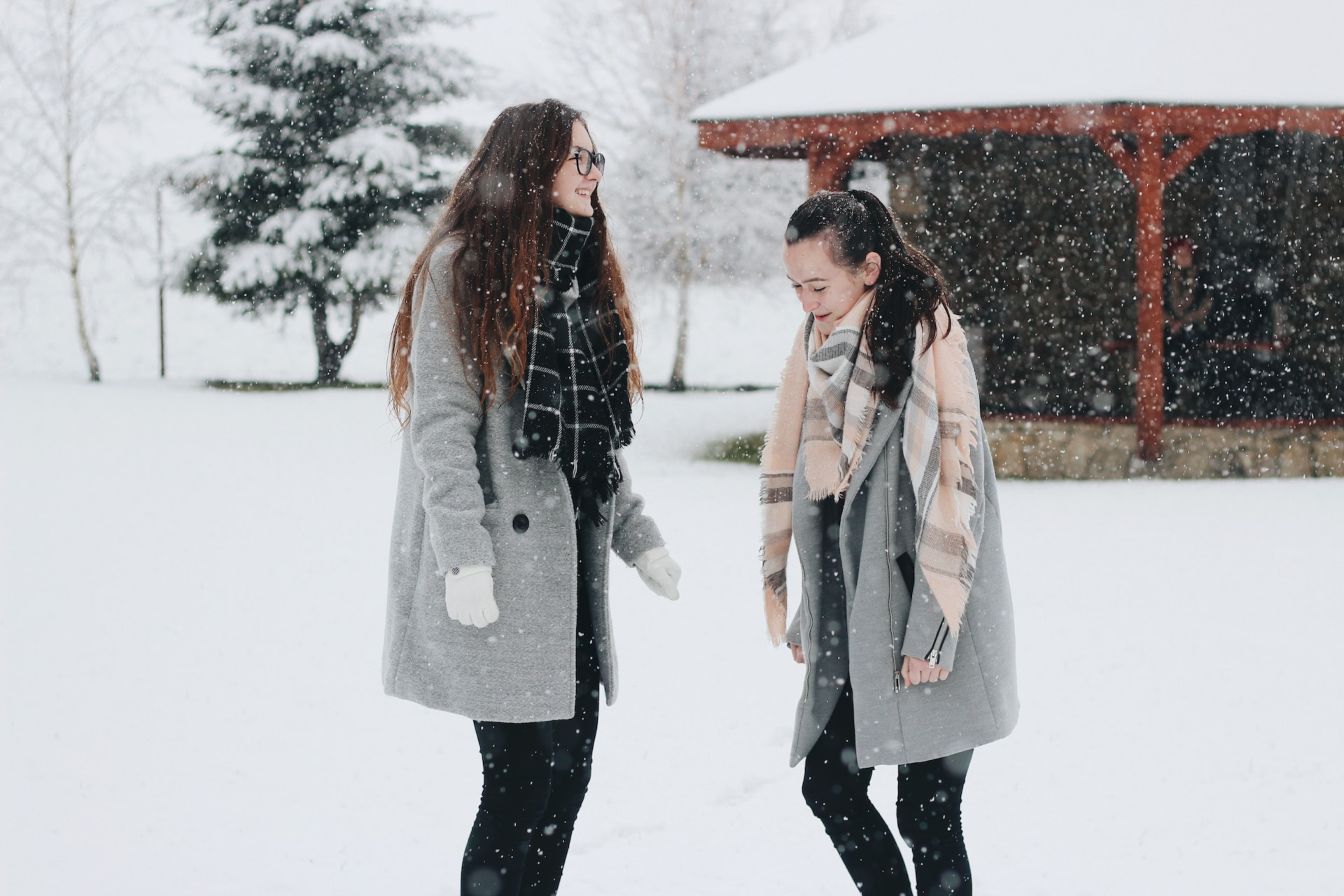 Two girls wearing warm clothing out in the snow