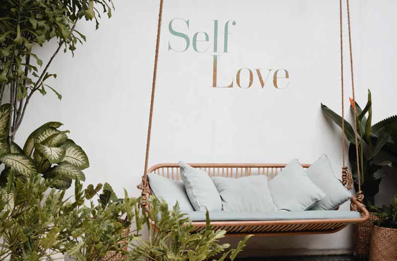 garden swing with pillows and writing on the wall self love