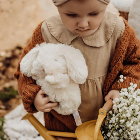 Little girl holding in her hands a white stuffed bunny plush toy and a basket of white flowers