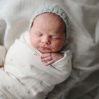 Newborn baby in her muslin baby swaddle blanket from Mushie