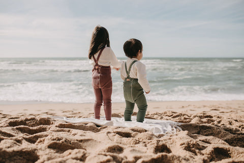 Two children standing on the sand and looking at the see.