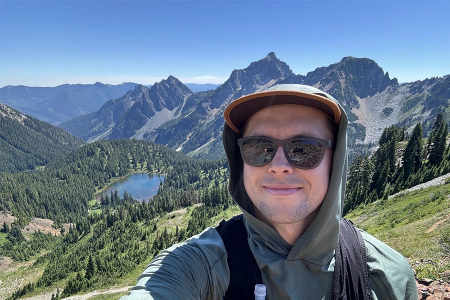 Zach taking a quick selfie with an alpine lake and mount peaks behind him.