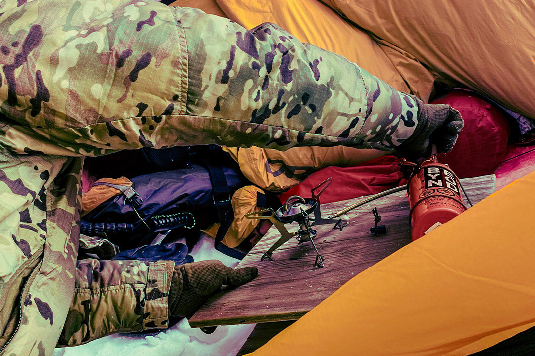 Person preparing an MSR stove with a custom base board inside the vestibule of a tent on a frozen lake.