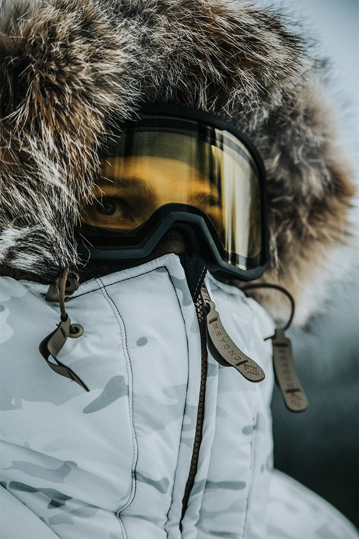 Person wearing the ArcticGate Parka with goggles in a snow background.
