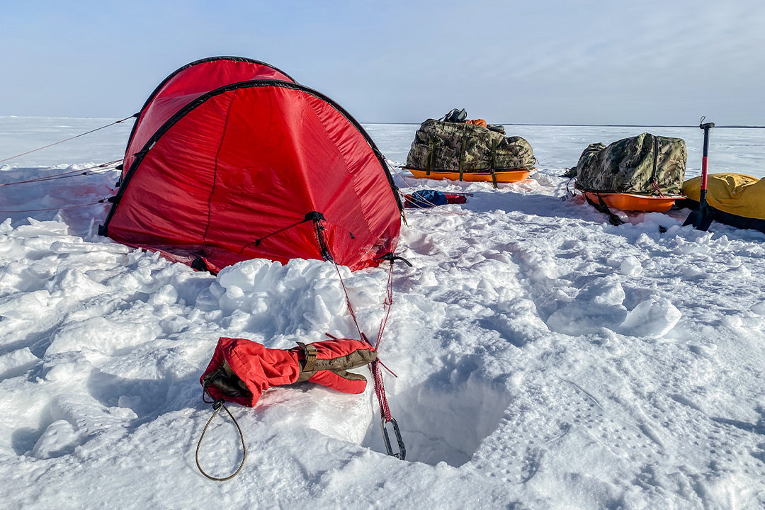 Arctic tent set up on a frozen lake with mitt and custom expedition sleds in the background.