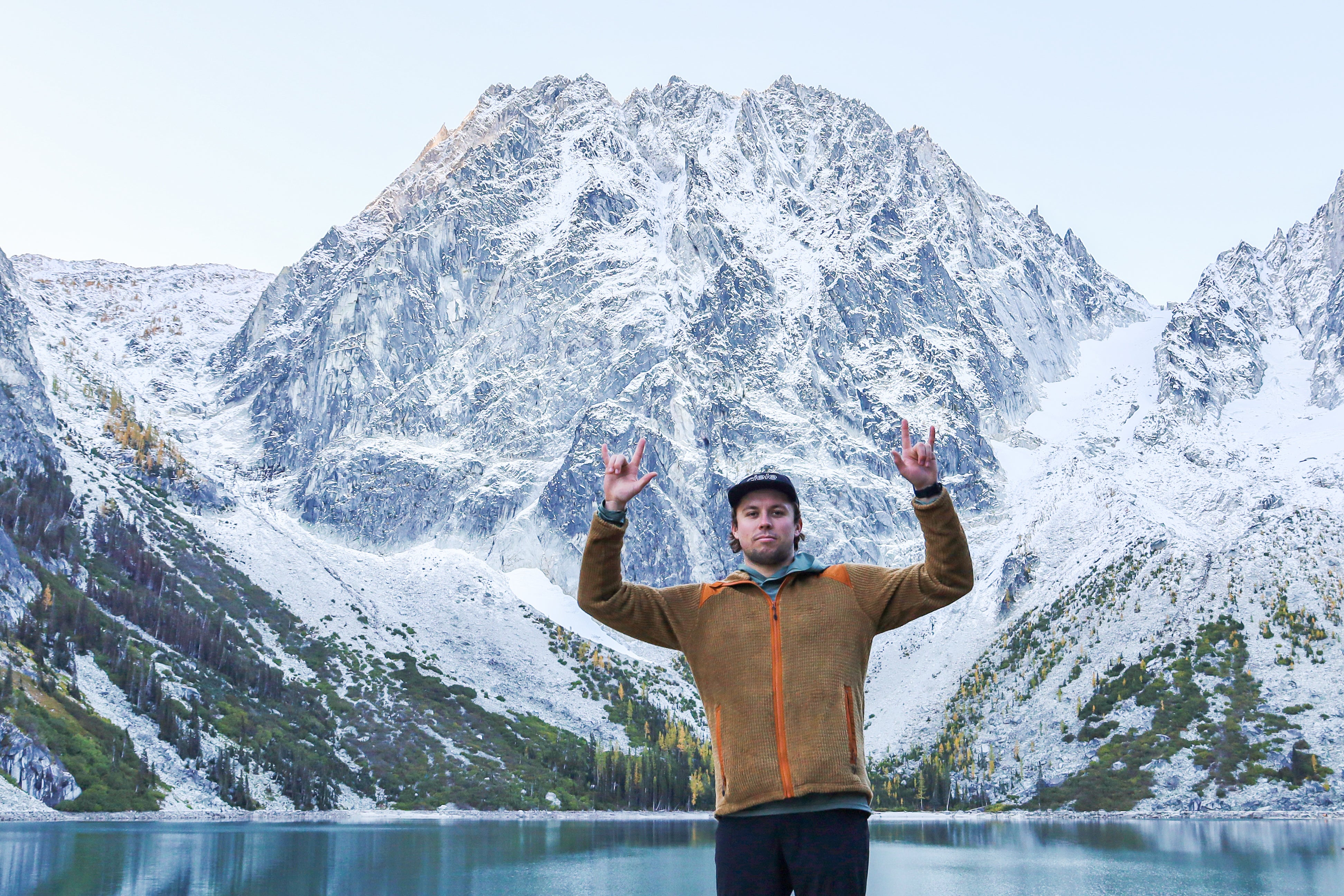 Hiker wearing the Beyond Alpha Aura Jacket while posing in front of a snowy mountain range.