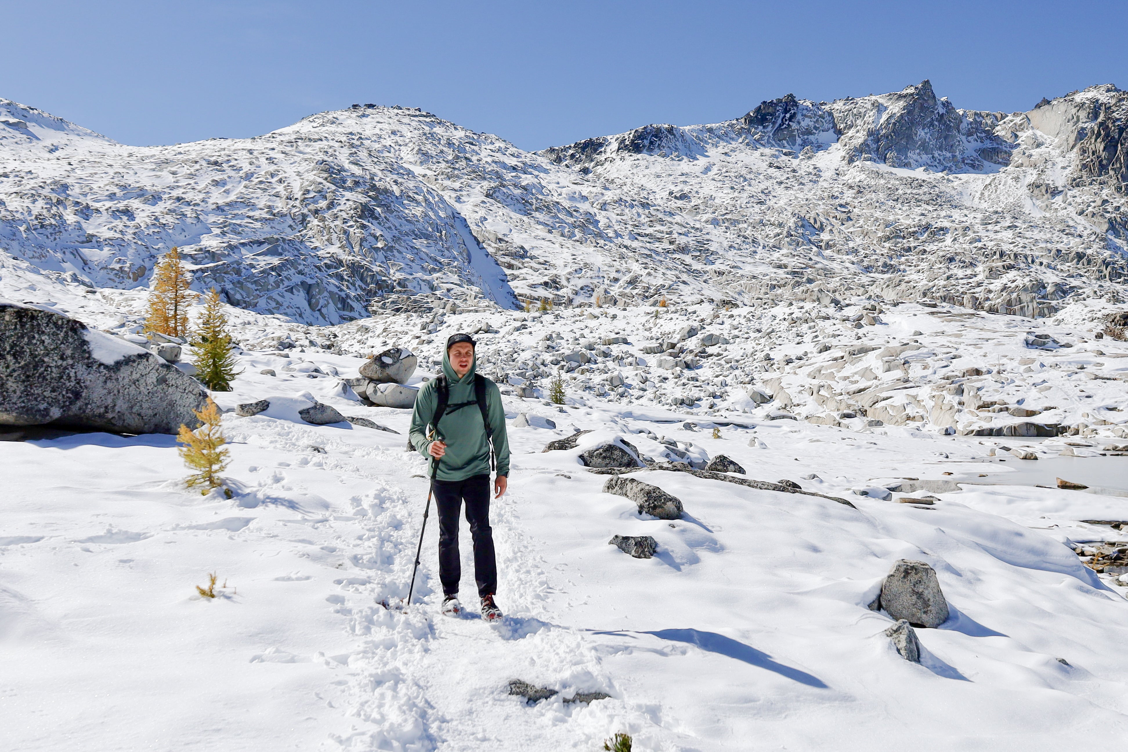 Hiker wearing Beyond Clothing Ascent-Glide Pants, a backpack and using poles to navigate through a foot of snow while on hike in the Enchantments.