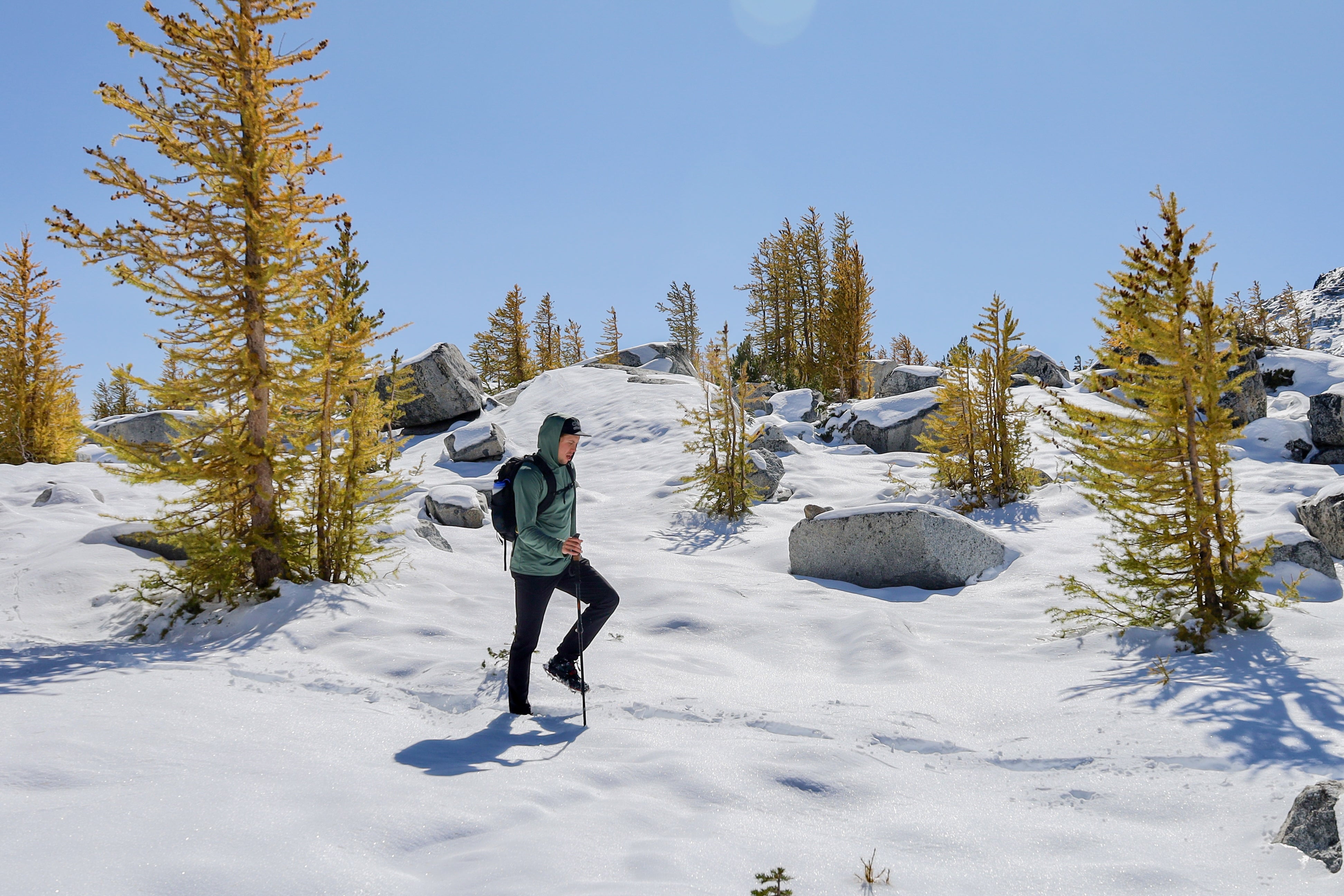 Hiker wearing Beyond Clothing Ascent-Glide Pants, a backpack and using poles to navigate through a foot of snow while on hike in the Enchantments.