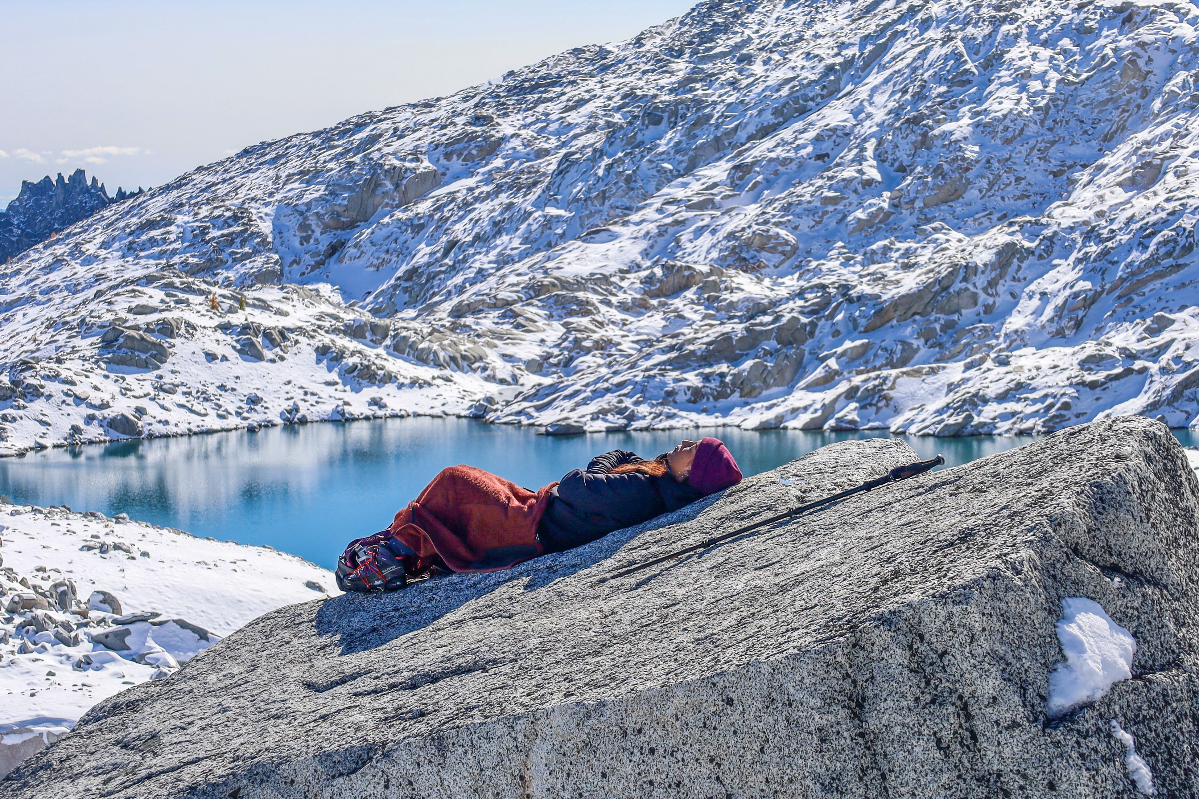 Hiker taking a break, resting on a rock over looking a lake with snow covered moutain side.