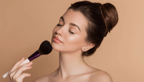 Beautyful girl with her makeup brush against a cream wall envying her makeup look.