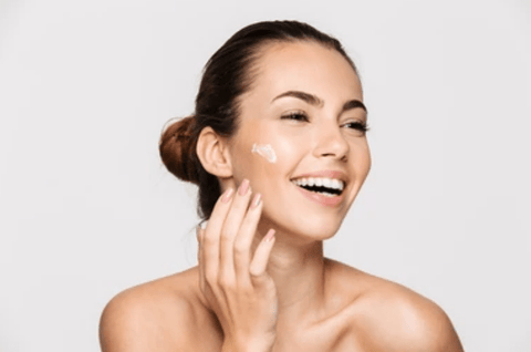 Women standing against a white background using facial cream on her face.