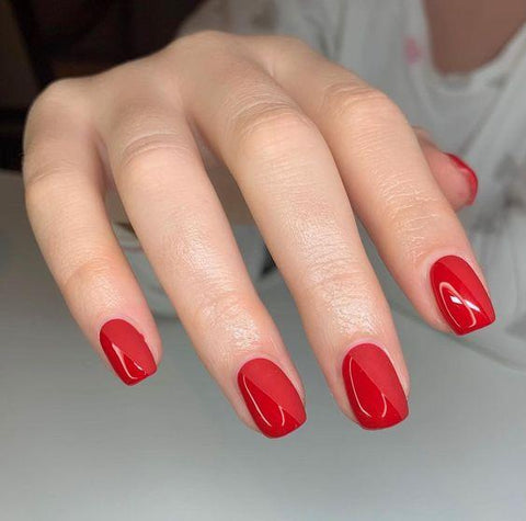 manicured nails with a red debelle top gloss red nail polish and a shady background