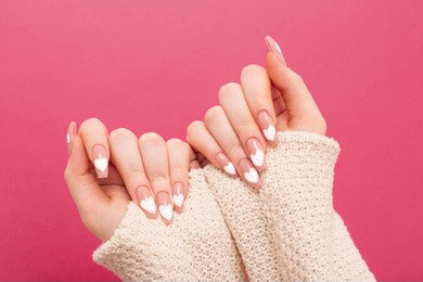 Girl with a Nail art resembling a Heart against a pink background wearing a cream sleave.