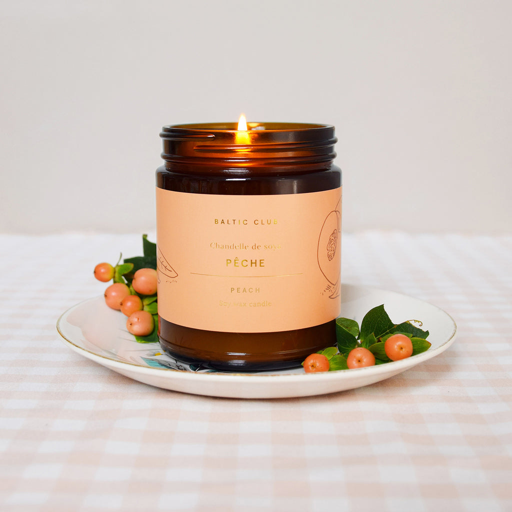 Peach Baltic Club Soy Candle burning on a table cloth