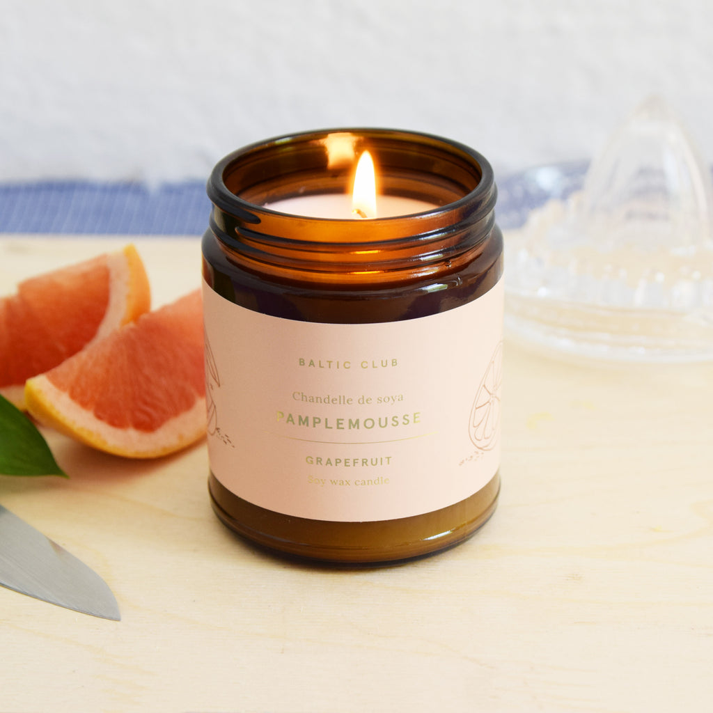 A Grapefruit candle burning in an amber jar on a table with fruits