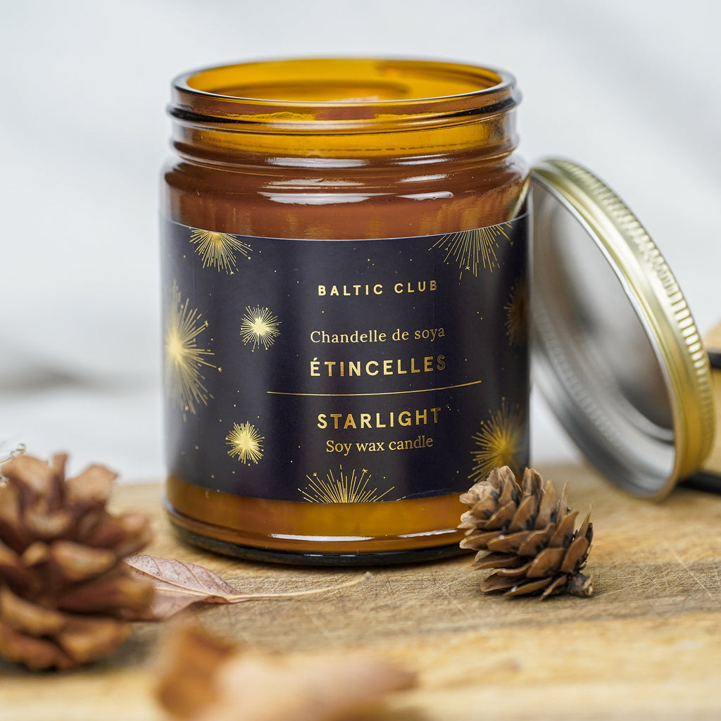 Baltic Club Starlight Soy candle with a wooden wick on a table with pine cones